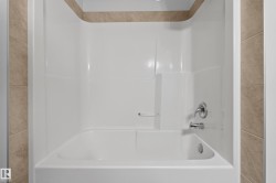 White bathtub and shower surround with integrated soap dish, featuring chrome fixtures and tile detailing - 