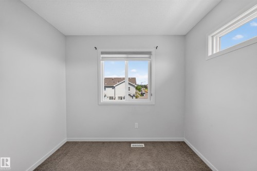 Bright secondary bedroom featuring neutral wall finishes, carpet flooring, and dual windows providing natural light and outdoor visibility - 1404 25 Avenue Nw, Edmonton, AB - Indoor Photo Showing Other Room