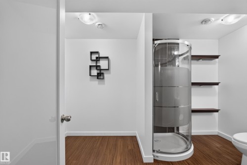Curved glass shower enclosure with a white base, three floating wood-finish shelves, and wood-finish flooring - 1404 25 Avenue Nw, Edmonton, AB - Indoor Photo Showing Bathroom