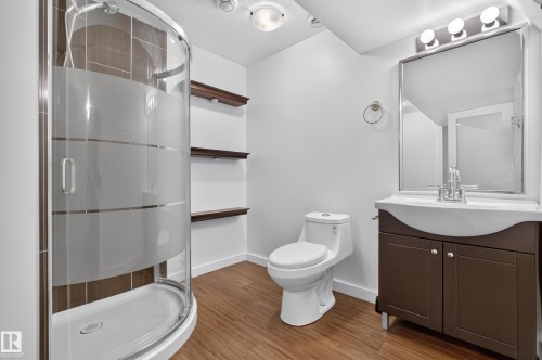 Curved glass shower enclosure with frosted bands, wood-finish flooring, dark wood vanity with integrated basin, framed wall mirror, and built-in wood shelving - 1404 25 Avenue Nw, Edmonton, AB - Indoor Photo Showing Bathroom