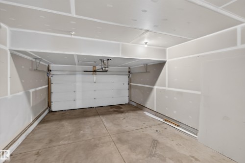 Concrete flooring, white overhead garage door, exposed drywall, overhead lighting fixtures, and an automatic garage door opener - 1404 25 Avenue Nw, Edmonton, AB - Indoor Photo Showing Garage