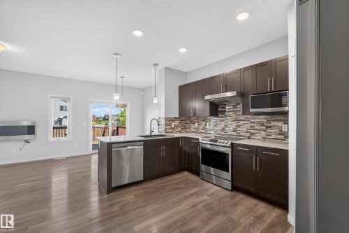 Open-concept kitchen featuring dark wood cabinetry, stainless steel appliances, a mosaic tile backsplash, and wood-finish flooring - 1404 25 Avenue Nw, Edmonton, AB - Indoor Photo Showing Kitchen With Upgraded Kitchen