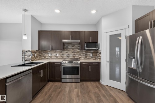 Contemporary kitchen featuring dark wood-finish cabinetry, stainless steel appliances, a mosaic tile backsplash, and light-toned countertops - 1404 25 Avenue Nw, Edmonton, AB - Indoor Photo Showing Kitchen With Double Sink With Upgraded Kitchen