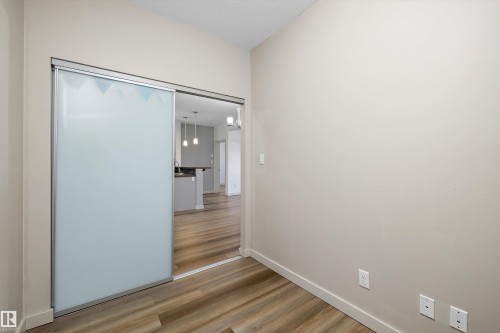Sliding frosted glass door with aluminum frame, wood-finish flooring, and neutral wall paint - #207 304 Amblside Li Sw Sw, Edmonton, AB - Indoor Photo Showing Other Room