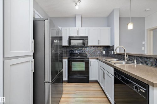 Kitchen featuring light-finish cabinetry, stainless steel refrigerator, black range, black microwave, and black dishwasher - #207 304 Amblside Li Sw Sw, Edmonton, AB - Indoor Photo Showing Kitchen With Double Sink