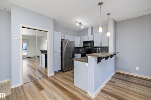 Well-appointed kitchen featuring light-colored cabinetry, stainless steel refrigerator, dark countertops, and a full backsplash - #207 304 Amblside Li Sw Sw, Edmonton, AB - Indoor Photo Showing Kitchen