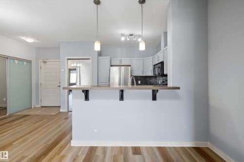 Kitchen bar with wood-finish countertop, stainless steel appliances, white cabinetry, and pendant lighting - #207 304 Amblside Li Sw Sw, Edmonton, AB - Indoor Photo Showing Kitchen With Upgraded Kitchen