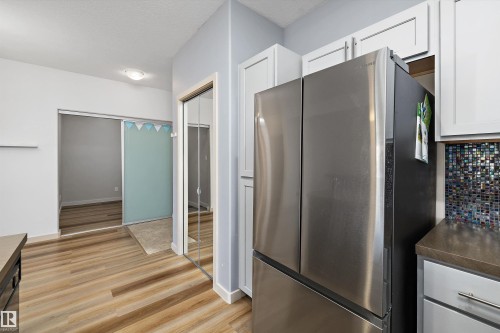 Wood-finish flooring throughout, white upper cabinetry, stainless steel refrigerator, and a mosaic tile backsplash - #207 304 Amblside Li Sw Sw, Edmonton, AB - Indoor Photo Showing Kitchen