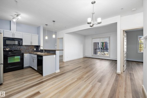 Kitchen with light gray cabinetry, built-in microwave, black appliances, and a mosaic tile backsplash - #207 304 Amblside Li Sw Sw, Edmonton, AB - Indoor Photo Showing Kitchen With Upgraded Kitchen