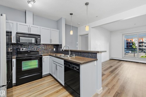 Kitchen featuring stainless steel refrigerator, black range, dishwasher, and microwave - #207 304 Amblside Li Sw Sw, Edmonton, AB - Indoor Photo Showing Kitchen With Double Sink