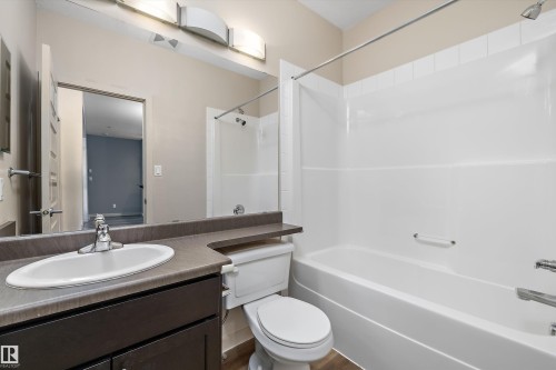 White porcelain sink with chrome faucet, dark wood-finish vanity, and a white bathtub with an integrated shower - #207 304 Amblside Li Sw Sw, Edmonton, AB - Indoor Photo Showing Bathroom