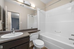 White porcelain sink with chrome faucet, dark wood-finish vanity, and a white bathtub with an integrated shower - 