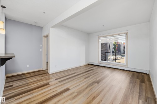 Wood-finish flooring, white walls, light gray accent wall, sliding glass door, and a built-in counter with pendant lighting - #207 304 Amblside Li Sw Sw, Edmonton, AB - Indoor