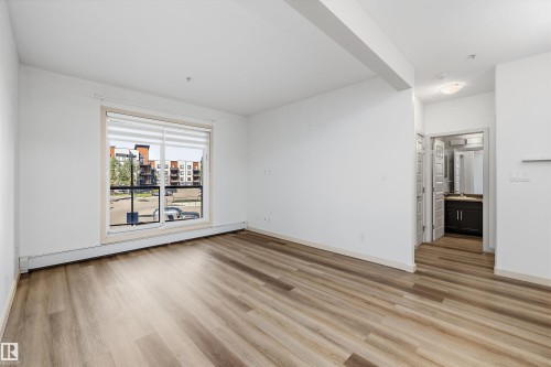 Wood-finish flooring, white walls, and a large window with blinds - #207 304 Amblside Li Sw Sw, Edmonton, AB - Indoor