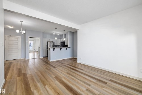 Open-concept living area with wood-finish flooring, a kitchen featuring light cabinetry, a peninsula with seating, and stainless steel appliances - #207 304 Amblside Li Sw Sw, Edmonton, AB - Indoor