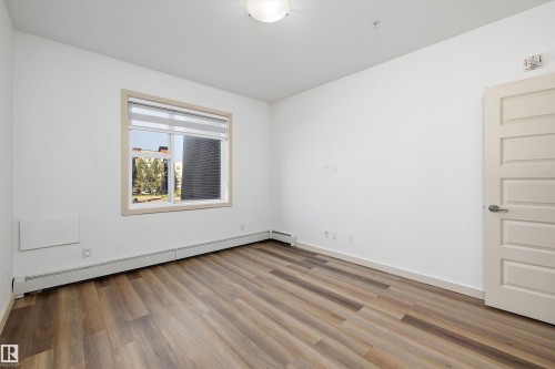 Wood-finish flooring, white paneled interior door, and a single window with blinds - #207 304 Amblside Li Sw Sw, Edmonton, AB - Indoor Photo Showing Other Room