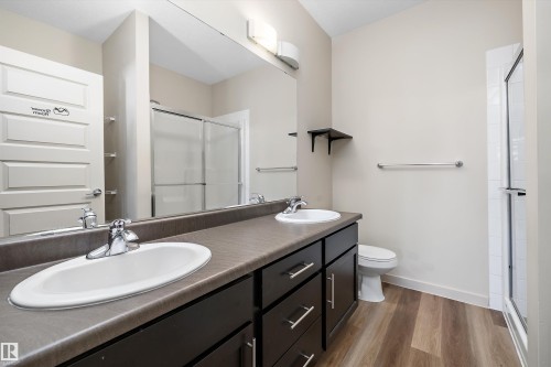 Dual vanity with integrated sinks, dark wood-finish cabinetry, a large wall-mounted mirror, and wood-finish flooring - #207 304 Amblside Li Sw Sw, Edmonton, AB - Indoor Photo Showing Bathroom