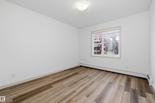 Wood-finish flooring with white walls and a large window - #207 304 Amblside Li Sw Sw, Edmonton, AB - Indoor Photo Showing Other Room