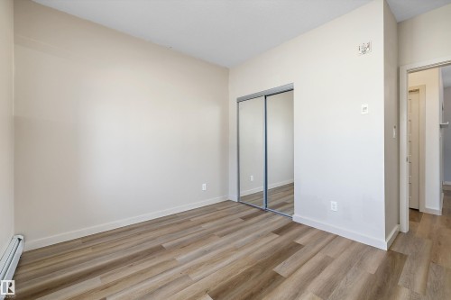 Wood-finish flooring, mirrored closet doors, and light-toned walls - #207 304 Amblside Li Sw Sw, Edmonton, AB - Indoor Photo Showing Other Room