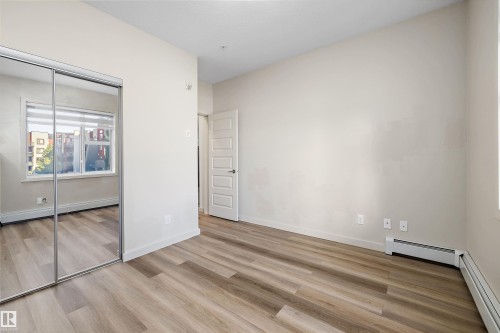 Neutral wall paint, wood-finish flooring, mirrored sliding closet doors, white window trim, and a five-panel interior door - #207 304 Amblside Li Sw Sw, Edmonton, AB - Indoor Photo Showing Other Room