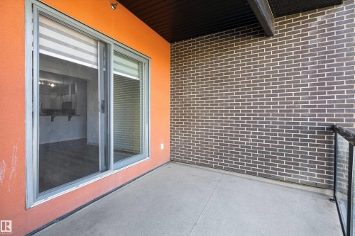 Concrete balcony with a dark brick wall and an orange stucco accent wall - #207 304 Amblside Li Sw Sw, Edmonton, AB - Outdoor With Exterior