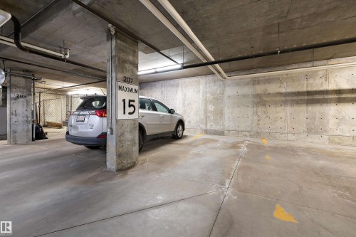 Concrete subterranean parking space with exposed concrete walls, structural columns, and overhead utility piping - #207 304 Amblside Li Sw Sw, Edmonton, AB - Indoor Photo Showing Garage