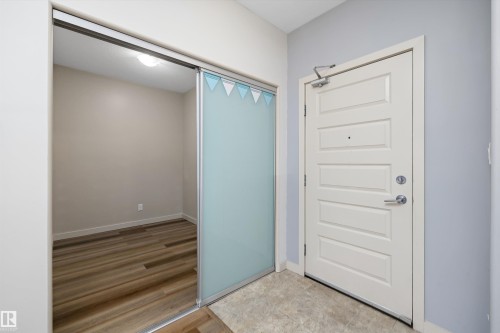 Entryway featuring a paneled door with polished hardware, a sliding frosted glass partition, and wood-finish flooring - #207 304 Amblside Li Sw Sw, Edmonton, AB - Indoor Photo Showing Other Room