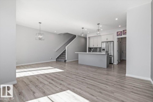Open-concept living area featuring wood-finish flooring, a kitchen island with seating, stainless steel appliances, and sleek pendant lighting - 1014 Daniels Loop Sw, Edmonton, AB - Indoor Photo Showing Kitchen With Upgraded Kitchen