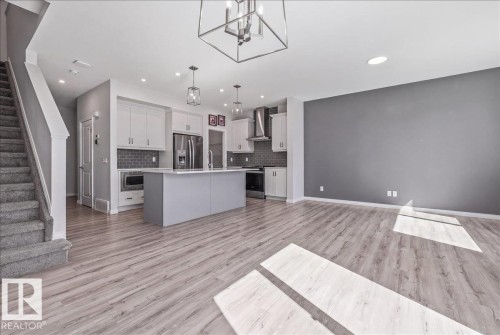 Contemporary open-concept interior featuring light wood-finish flooring, a modern kitchen island with pendant lighting, stainless steel appliances, and a carpeted staircase - 1014 Daniels Loop Sw, Edmonton, AB - Indoor Photo Showing Kitchen With Upgraded Kitchen