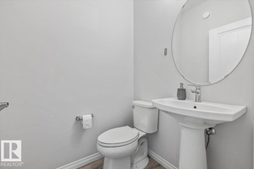 Pedestal sink with chrome faucet, circular wall mirror, and toilet - 1014 Daniels Loop Sw, Edmonton, AB - Indoor Photo Showing Bathroom