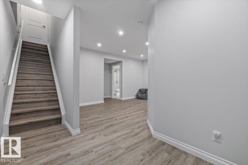 Wood-finish flooring, recessed lighting, neutral wall tones, and a built-in staircase with a white handrail - 1014 Daniels Loop Sw, Edmonton, AB - Indoor Photo Showing Other Room
