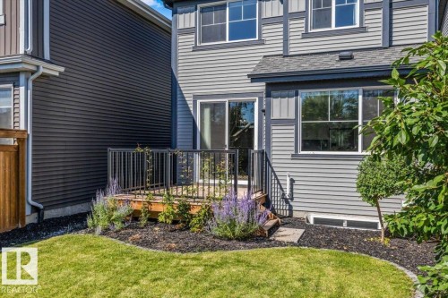 Rear exterior featuring a wood deck with black metal railing, sliding glass door, and a manicured lawn - 1014 Daniels Loop Sw, Edmonton, AB - Outdoor