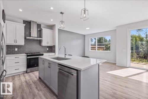 Modern kitchen featuring stainless steel appliances, a center island with sink, white shaker cabinetry, and wood-finish flooring - 1014 Daniels Loop Sw, Edmonton, AB - Indoor Photo Showing Kitchen With Upgraded Kitchen