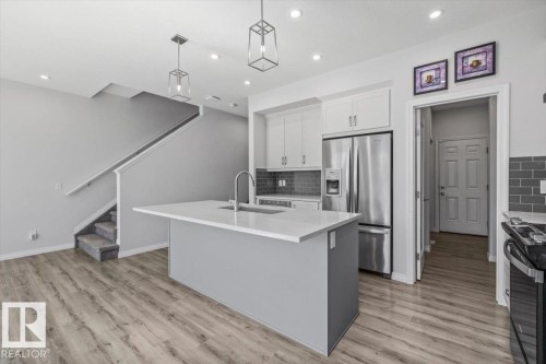 White kitchen cabinetry with stainless steel appliances, gray subway tile backsplash, and a central island with a sink - 1014 Daniels Loop Sw, Edmonton, AB - Indoor Photo Showing Kitchen With Upgraded Kitchen