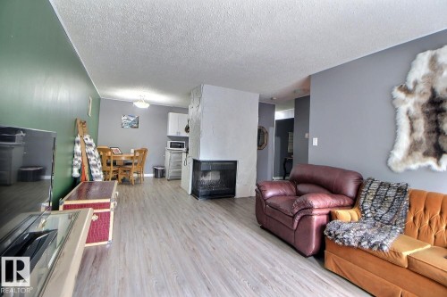 Wood-finish flooring throughout, complemented by a stone-clad fireplace - #304 14004 26 St Nw, Edmonton, AB - Indoor Photo Showing Living Room With Fireplace