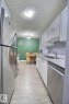 Galley kitchen featuring stainless steel appliances, white cabinetry, light countertops, and wood-finish flooring - #304 14004 26 St Nw, Edmonton, AB  - Indoor Photo Showing Kitchen With Double Sink 
