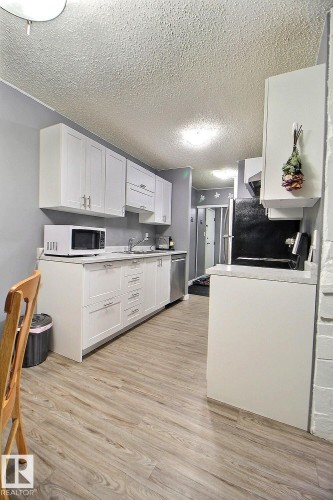 Kitchen featuring white shaker-style cabinetry, stainless steel dishwasher, light wood-finish flooring, white countertops, and a ceiling-mounted light fixture - #304 14004 26 St Nw, Edmonton, AB - Indoor Photo Showing Kitchen