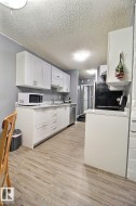 Kitchen featuring white shaker-style cabinetry, stainless steel dishwasher, light wood-finish flooring, white countertops, and a ceiling-mounted light fixture - 