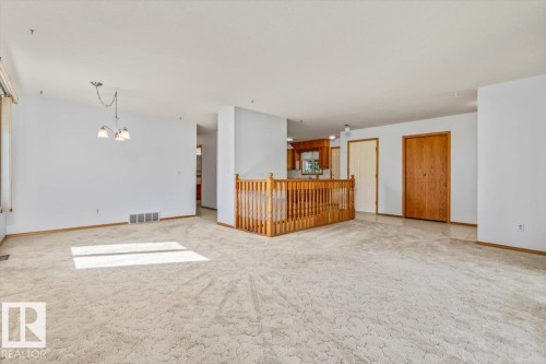 Open-concept living area with carpet flooring, a natural wood-finish staircase railing, and a dining light fixture - 4427 Payne Avenue, Onoway, AB - Indoor