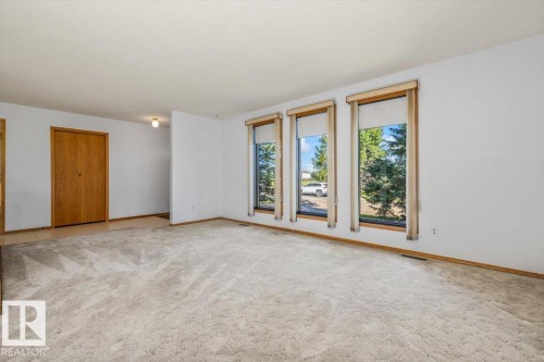 Carpeted flooring, three large windows with wood-finish trim, wood-finish bi-fold doors, and a flush mount ceiling light fixture - 4427 Payne Avenue, Onoway, AB - Indoor Photo Showing Other Room