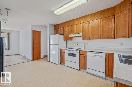 Kitchen with wood cabinetry, white appliances, and a double basin stainless steel sink - 4427 Payne Avenue, Onoway, AB - Indoor Photo Showing Kitchen With Double Sink