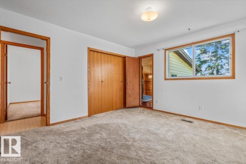 Textured carpet flooring, window with wood trim, wood-finish bi-fold closet doors, wood-finish interior door frames, flush-mount ceiling light fixture - 4427 Payne Avenue, Onoway, AB - Indoor Photo Showing Other Room