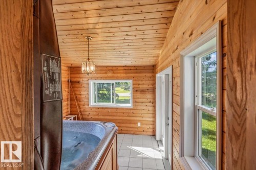 Wood-paneled room featuring a built-in hot tub, white tile flooring, double-pane windows, a brass light fixture, and a vaulted wood-paneled ceiling - 4427 Payne Avenue, Onoway, AB - Indoor Photo Showing Other Room