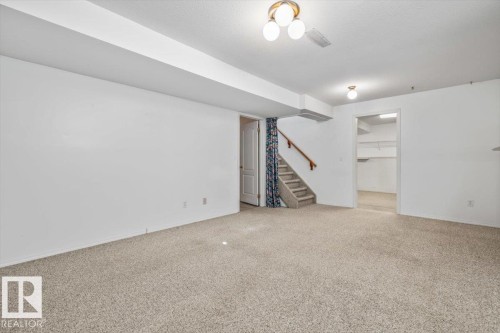 Expansive carpeted area with white walls, a built-in staircase with wood handrail, and overhead lighting fixtures - 4427 Payne Avenue, Onoway, AB - Indoor Photo Showing Other Room