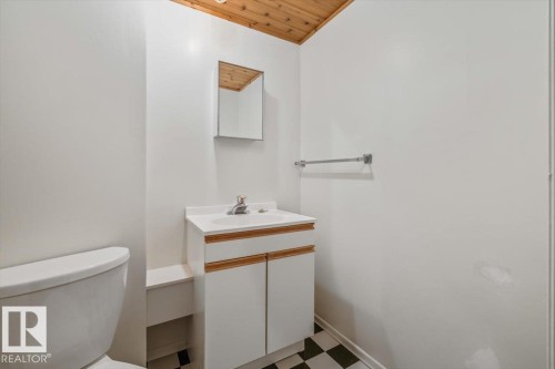 Wood-paneled ceiling, white walls, checked flooring, white vanity with integrated sink, and wall-mounted mirror - 4427 Payne Avenue, Onoway, AB - Indoor Photo Showing Bathroom