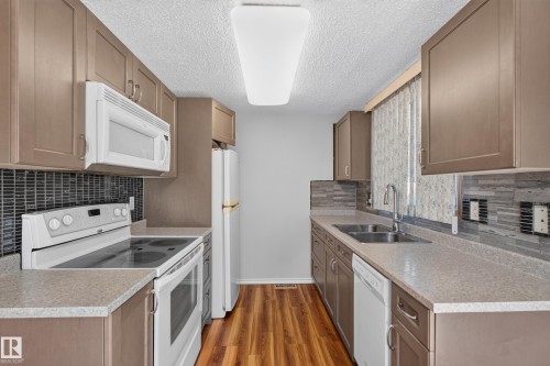 Galley kitchen with wood-finish flooring, light-toned countertops, and dual basin stainless steel sink - 23 Willowdale Place Nw, Edmonton, AB 