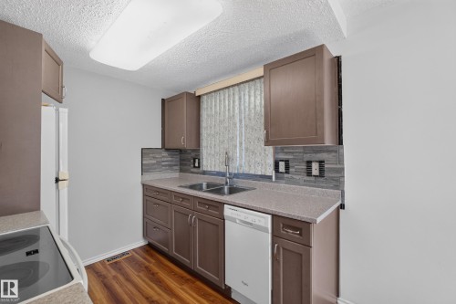 Functional kitchen featuring wood-finish flooring, brown cabinetry, a double basin sink, and a tiled backsplash - 23 Willowdale Place Nw, Edmonton, AB 