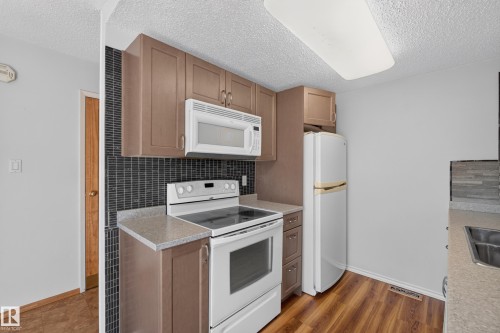 Kitchen featuring wood-finish flooring, full-height tile backsplash, integrated microwave, and built-in cabinetry - 23 Willowdale Place Nw, Edmonton, AB 