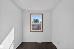 Warm-toned window trim, dark wood-finish flooring, white painted walls, and a textured ceiling - 