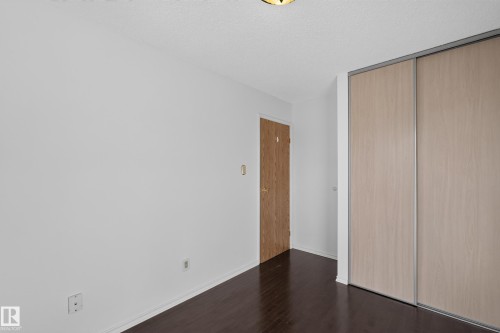 Hardwood-finish flooring with white baseboards, a light wood-finish door, and integrated sliding closet doors with metal trim - 23 Willowdale Place Nw, Edmonton, AB 